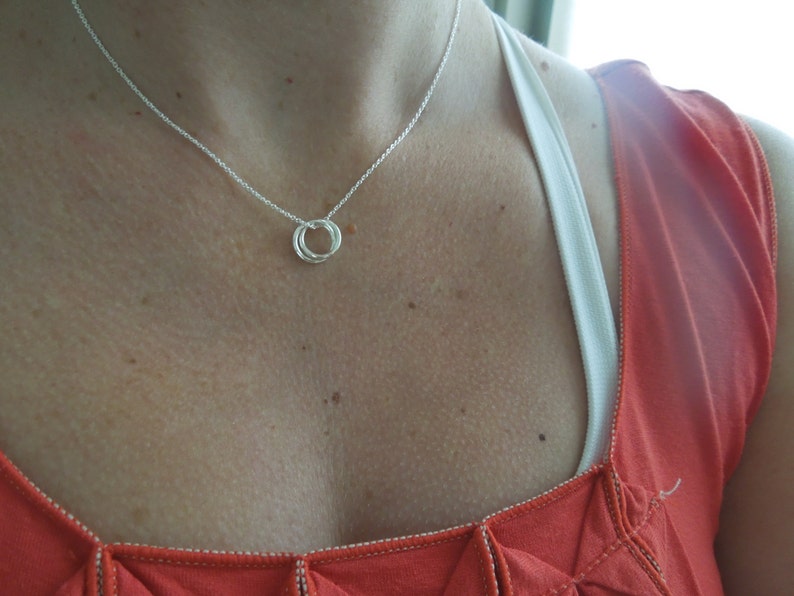 May include: A silver necklace with a simple, twisted circle pendant. The necklace is worn by a person with a red shirt.