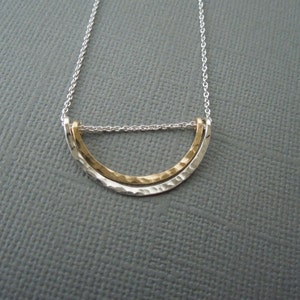 May include: A silver chain necklace with a gold and silver hammered half-circle pendant.
