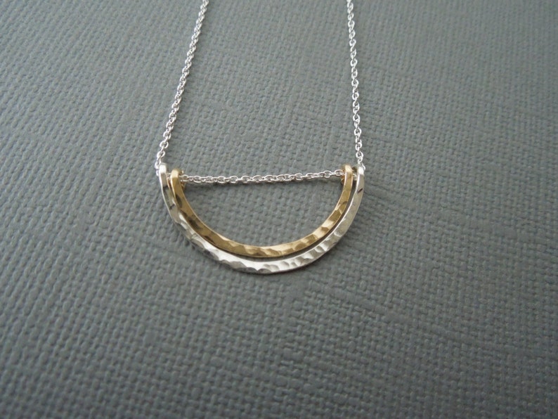 May include: A silver chain necklace with a gold and silver hammered half-circle pendant.
