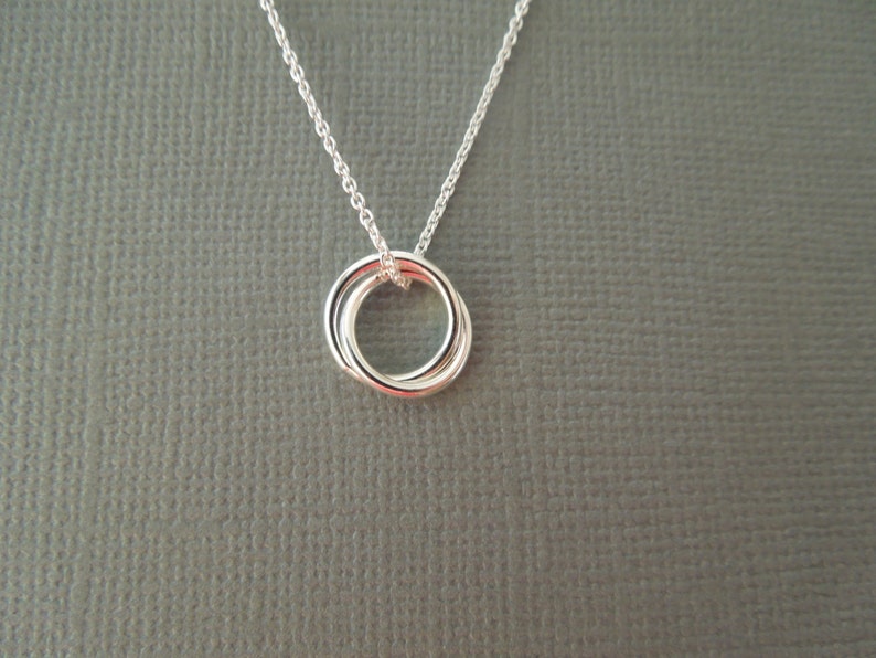 May include: Silver necklace with a three-ring pendant. The rings are intertwined and form a circle.