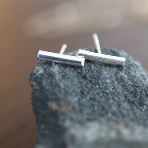 May include: A pair of silver bar stud earrings. The earrings are simple and minimalist, and they are perfect for everyday wear.