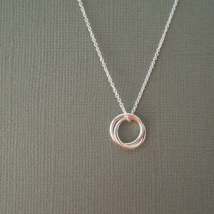May include: A silver necklace with a delicate pendant featuring three interlocking rings.