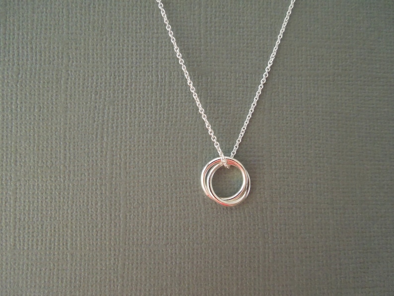 May include: A silver necklace with a delicate pendant featuring three interlocking rings.