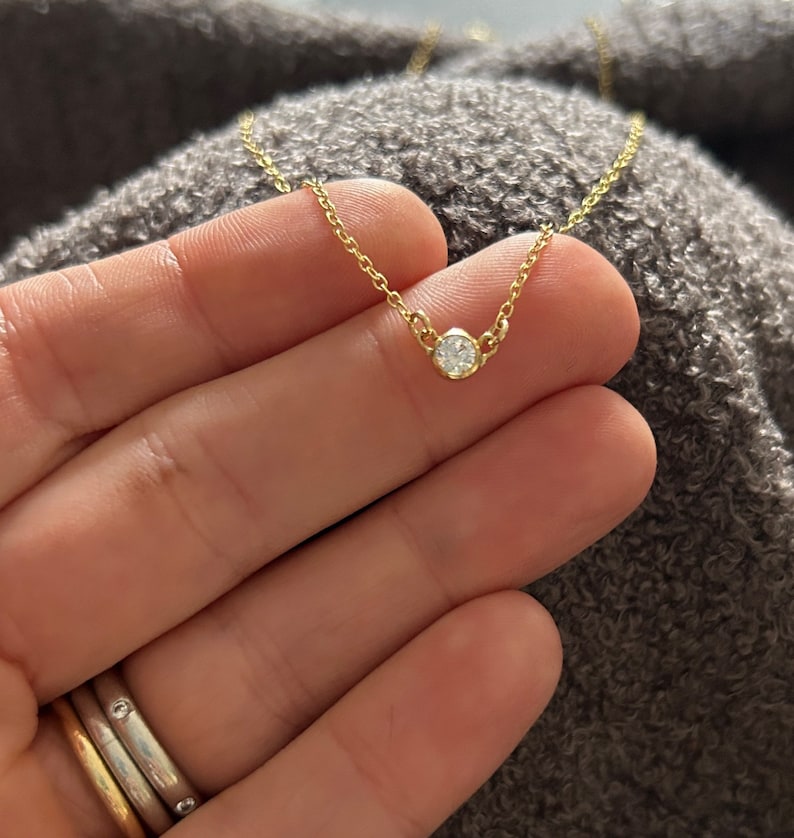 K&ouml;nnte beinhalten: Eine zarte goldene Kettenkette mit einem kleinen, runden, klaren Diamantenanh&auml;nger.