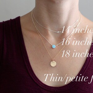 May include: Three gold necklaces with different lengths: 14 inches, 16 inches, and 18 inches. The necklaces are layered on a person with a thin/petite frame wearing a burgundy tank top.