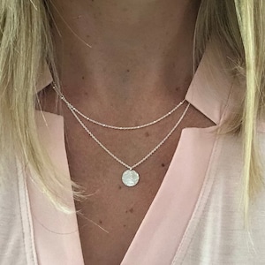 May include: A silver necklace with a delicate chain and a small, round pendant. The pendant has a hammered texture and is a simple, minimalist design.