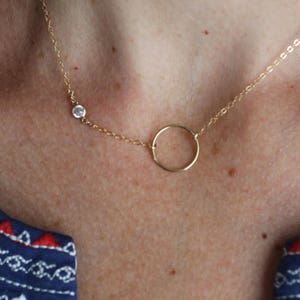 Puede incluir: Un collar de cadena de oro con un peque&ntilde;o colgante circular y un solo acento de piedra clara.