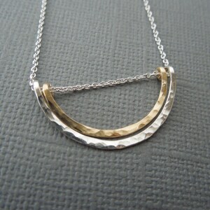 May include: A silver chain necklace with a gold and silver pendant. The pendant is a hammered, curved shape.
