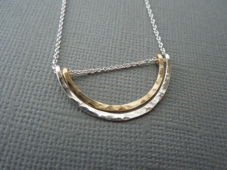 May include: A silver chain necklace with a gold and silver pendant. The pendant is a hammered, curved shape.