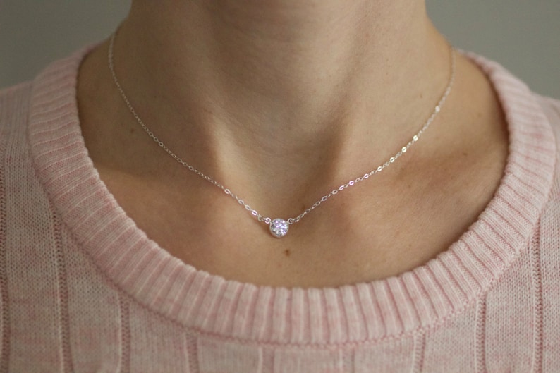 May include: A delicate silver chain necklace with a single, small, clear cubic zirconia pendant.