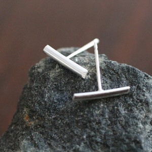 May include: A pair of silver bar stud earrings. The earrings are simple and minimalist, with a straight bar design.