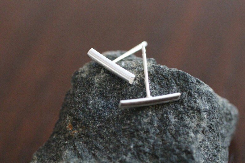 May include: A pair of silver bar stud earrings. The earrings are simple and minimalist, with a straight bar design.