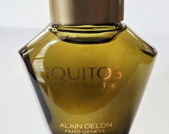 Può includere: Un flacone di profumo in vetro con una tonalità verde oliva scuro e una forma ampia e sfaccettata. Il flacone presenta un tappo dorato e la scritta dorata IQUITOS EAU DE TOILETTE e ALAIN DELON PARIS-GENEVE stampata sulla superficie del vetro.