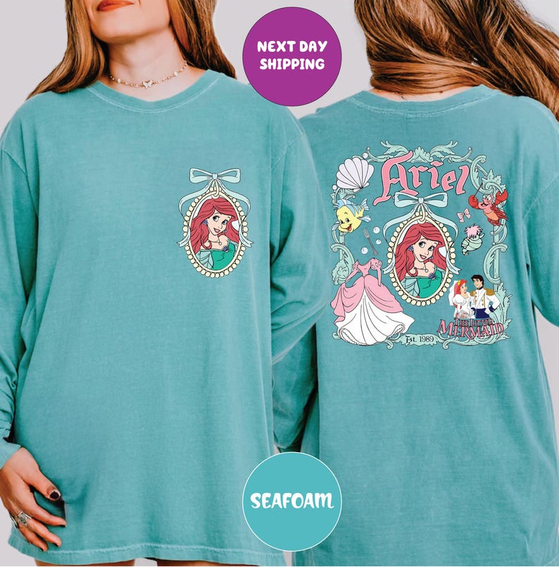a woman wearing a teal long-sleeved shirt with a design of Ariel from the Disney movie "The Little Mermaid". The design includes Ariel's face, a mermaid, and various other characters from the film. The shirt also has a "Next day shipping" label, indicating that the shirt is available for immediate purchase.