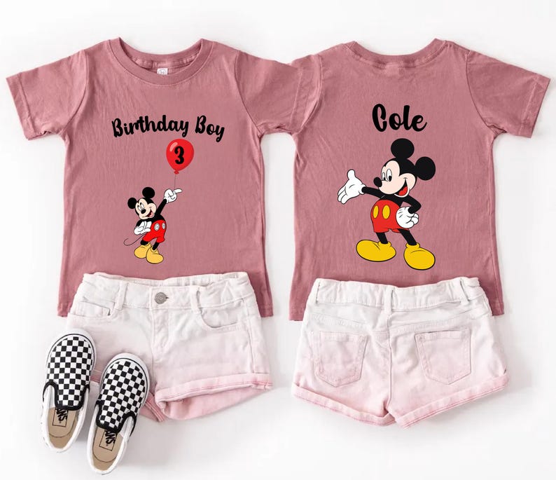 a pink t-shirt with a Mickey Mouse design and the text "Birthday Boy 3" printed on it, along with a pair of white shorts and checkered shoes.