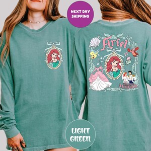A woman wearing a green long-sleeved shirt with a graphic of Ariel from the Disney movie "The Little Mermaid".