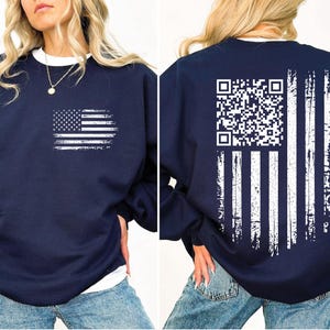 May include: Navy blue sweatshirt featuring a distressed white American flag graphic on the front. The back of the sweatshirt displays a QR code and vertical white stripes, also distressed. The sweatshirt has a crew neck and long sleeves.