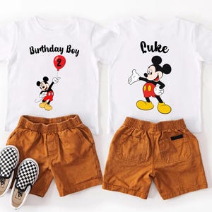 a pair of white t-shirts with Mickey Mouse designs, brown shorts, and a pair of black and white checkered shoes.