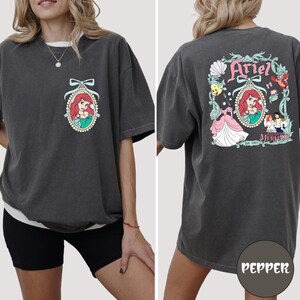 A woman wearing a gray t-shirt with a graphic of the Disney character Ariel from The Little Mermaid.