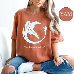 a woman sitting on a toilet wearing a t - shirt with a dragon on it