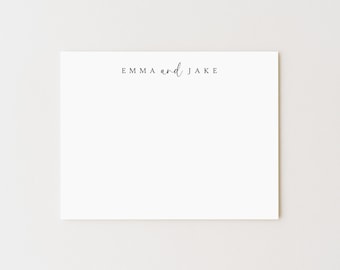 May include: A white stationery card with the names "EMMA and JAKE" printed in a delicate, black script at the top. The card is rectangular and set against a neutral background, suitable for personalized notes or announcements.