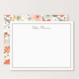 May include: A white stationery set with a floral design. The stationery features a white card with a green border and the name "Ella Marie" in cursive. The envelope has a colorful floral pattern with orange, pink, and green flowers.