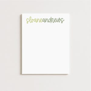 May include: A white notepad with the name "sloaneandrews" written in a light green script across the top. The notepad is rectangular and centered on a white background.