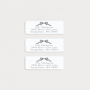 May include: Three rectangular white address labels with a gray bow design at the top. Each label has the name "Ella Thompson" and address details: 3098 River view Lane, Snoqualmie, WA 98065.