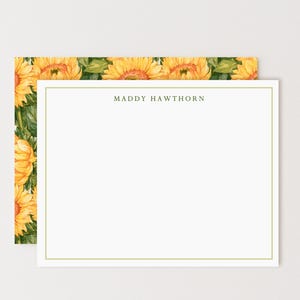 May include: A rectangular stationery card featuring a white center with a thin gold border and the name MADDY HAWTHORN printed in dark text at the top. The card is layered over a background pattern of yellow sunflowers and green leaves.