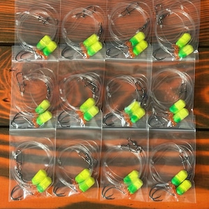May include: Twelve clear plastic bags each containing a fishing lure with two yellow and green beads and a black hook.