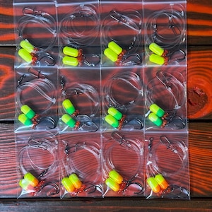 May include: Twelve clear plastic bags each containing two yellow and green fishing lures with red accents. The lures are attached to a clear fishing line.