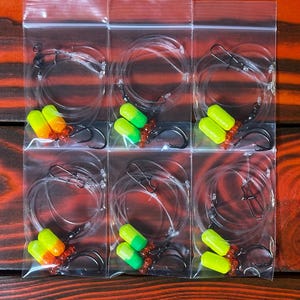 May include: Six clear plastic bags each containing two yellow and red fishing lures with hooks. The lures are attached to a clear fishing line.