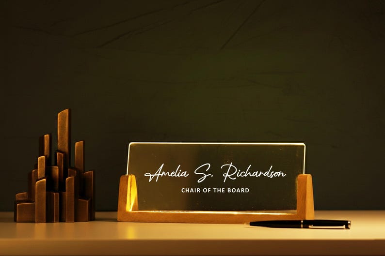 May include: A desk nameplate with the name "Amelia S. Richardson" and the title "CHAIR OF THE BOARD" in elegant script. The nameplate is in a wooden holder, with a pen and a decorative sculpture nearby.