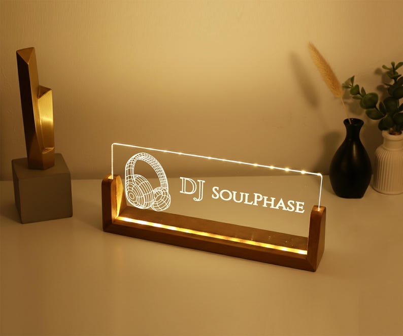 May include: A lighted DJ sign with the text "DJ SOULPHASE" and a headphone graphic. The sign is made of clear acrylic and sits in a wooden base. A gold sculpture and vases are in the background.