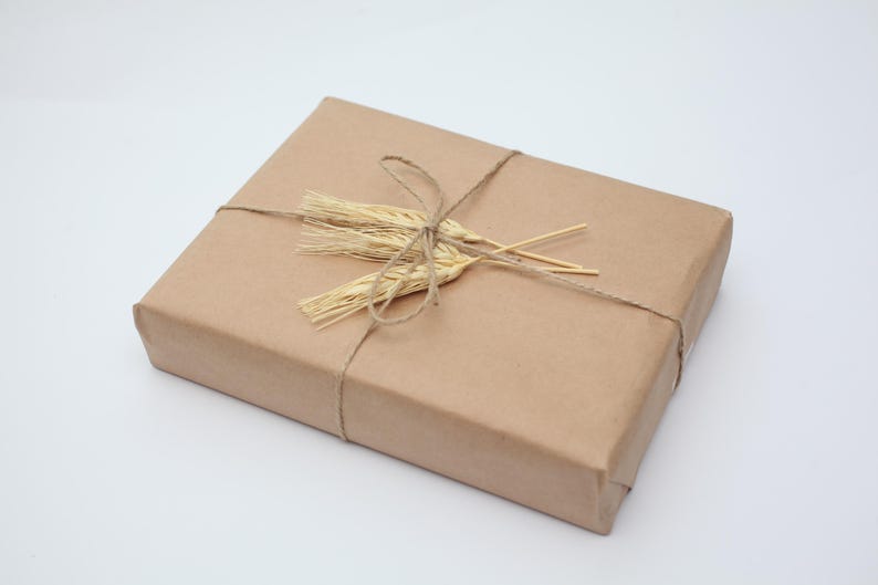 May include: A rectangular package wrapped in brown paper, tied with twine, and adorned with dried wheat stalks. The package is presented on a white background, creating a rustic and natural aesthetic.