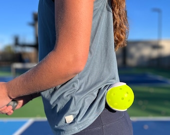 May include: A person wearing a blue tank top and black pants with a yellow and white pickleball attached to their back.
