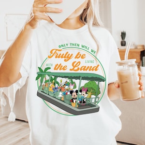 Könnte beinhalten: Weißes T-Shirt mit einem farbenfrohen Grafikdesign eines Boots mit Disney-Figuren und dem Text "Only Then Will We Truly Be Living With the Land" in einem Kreis. Das Shirt hat eine lockere, übergroße Passform.