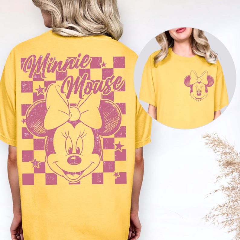 May include: Yellow t-shirt featuring a distressed Minnie Mouse graphic. The design includes a large Minnie Mouse face with a bow, set against a pink and purple checkered background. The text "Minnie Mouse" is above the character.
