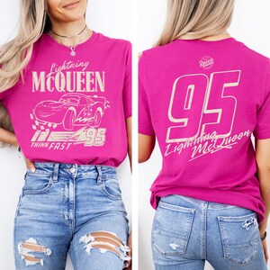 May include: A magenta t-shirt featuring Lightning McQueen graphics. The front displays the character's name and image, along with the number 95. The back of the shirt has a large number 95 and the Lightning McQueen name. The shirt is paired with blue jeans.