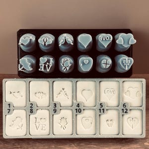 May include: A set of heart-shaped soap molds in a black tray, and a set of rectangular soap molds in a gray tray. The soap molds have various designs, including hearts, birds, and the word "LOVE".