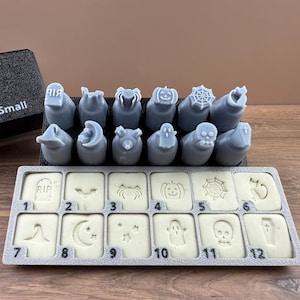 May include: A set of gray Halloween-themed stamps and matching imprints. The stamps feature designs like a tombstone, bat, spider, pumpkin, and skull. The set includes the text "print STUDIO" and "ween (A) Small".