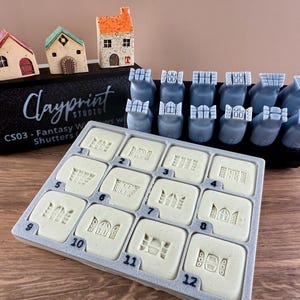 Könnte beinhalten: Eine Sammlung von Bastelwerkzeugen zum Thema Fantasy. Das Set enthält Miniaturhausmodelle, Stempel und eine Schale mit detaillierten Stempeldesigns. Der Text "Clayprint Studio" und "CS03 - Fantasy Windows Shutters" ist sichtbar.