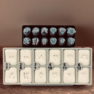 May include: Two trays of soap stamps with various designs. The top tray holds blue heart-shaped soaps with embossed images and the word "LOVE". The bottom tray contains rectangular soaps with heart, bird, and floral designs, and the word "LOVE".