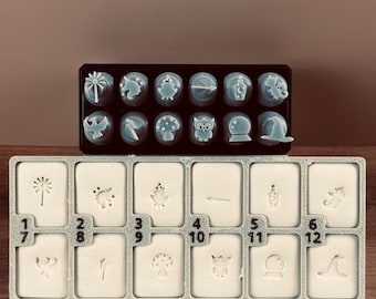Könnte beinhalten: Zwei Tabletts mit Bastelstempeln. Das obere Tablett enthält zwölf hellblaue Stempel mit verschiedenen Designs, darunter eine Palme, ein Pilz und eine Eule. Das untere Tablett hat zwölf weiße Stempel mit entsprechenden Designs und Nummern.