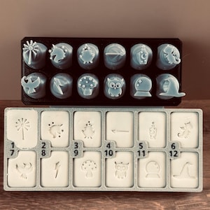 May include: Two trays of light blue wax melts and molds. The top tray holds round melts with various designs, including a unicorn, owl, and mushroom. The bottom tray has rectangular molds with matching designs and numbers.