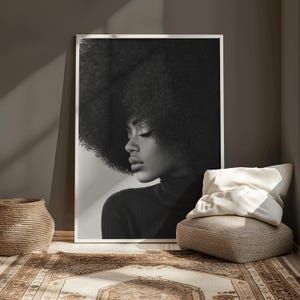 May include: Black and white portrait of a person with an afro hairstyle. The person is wearing a black turtleneck sweater and looking down.