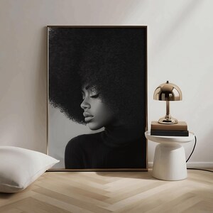 May include: Black and white portrait of a woman with an afro hairstyle wearing a black turtleneck sweater. The portrait is framed and hanging on a white wall.