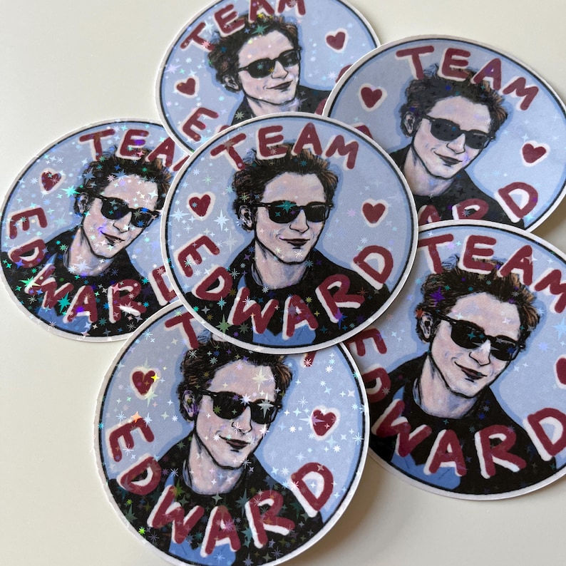 May include: A set of eight round stickers with a blue background and white glitter. Each sticker features a cartoon illustration of a man with dark hair and sunglasses. The text "Team Edward" is written in red around the edge of each sticker.