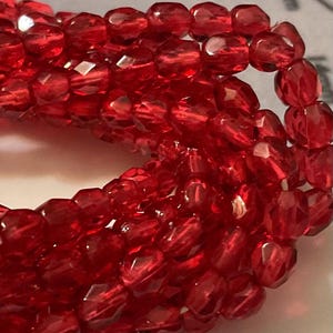Op de afbeelding: Een streng rode gefacetteerde glazen kralen. De kralen zijn klein en rond, met een glanzende afwerking.