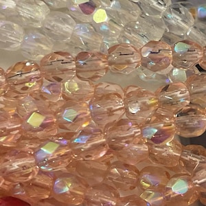 Op de afbeelding: Een streng iriserende roze glazen kralen. De kralen zijn gefacetteerd en hebben een licht onregelmatige vorm. De kralen zijn geregen op een doorzichtige draad.